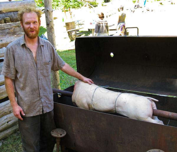 a man standing by a large smoker which contains a pig on a spit ready for roasting