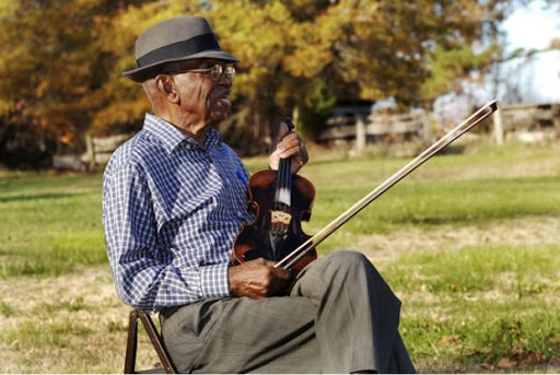 Joe Thompson seated outside playing fiddle in his nineties