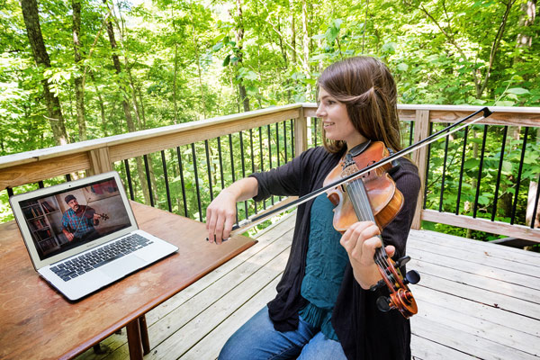 Fiddle student learning watching online instructional fiddle lessons video on a laptop outdoors